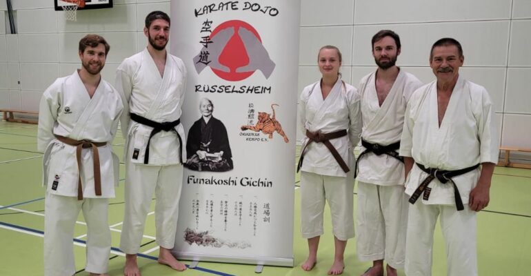 Unsere Karateka mit Meister Lothar Ratschke neben einem Aufsteller des VUnsere Karateka mit Meister Lothar Ratschke neben einem Aufsteller des Vereins in der Halleereins